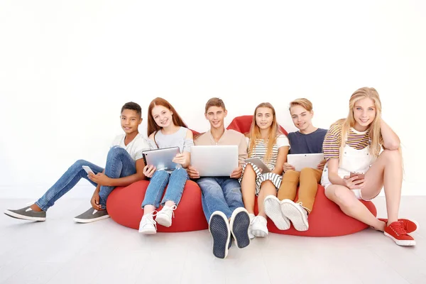 Adolescentes con aparatos modernos sentados en el salón cerca de la pared de luz — Foto de Stock