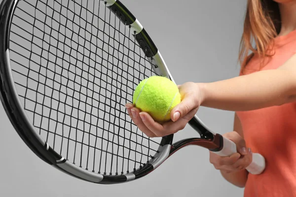 Woman with tennis racket and ball on grey background