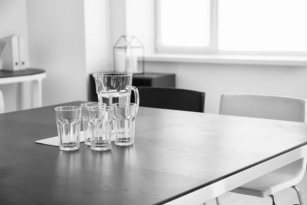 Big table with glasses and jug in light room — Stock Photo, Image