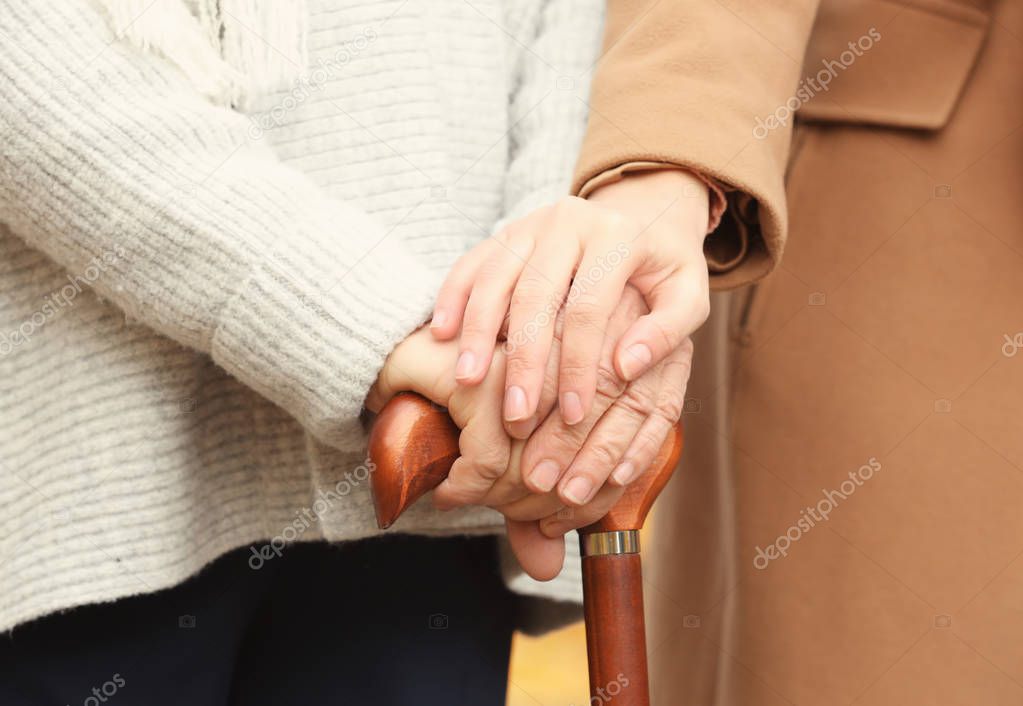 Young caregiver supporting senior woman with cane, closeup