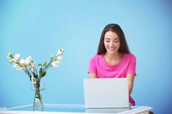 Jovem mulher usando laptop enquanto se senta na mesa contra a parede de cores — Fotografia de Stock