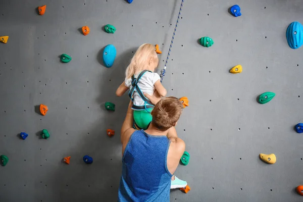 Instructeur helpt kleine meisje klim muur in sportschool — Stockfoto