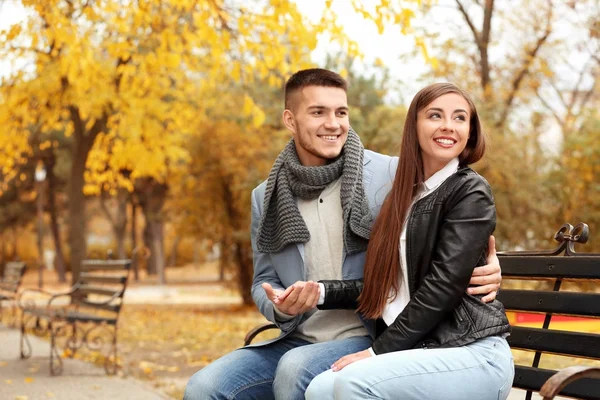 Pareja joven sentada en el banco en el parque de otoño — Foto de Stock