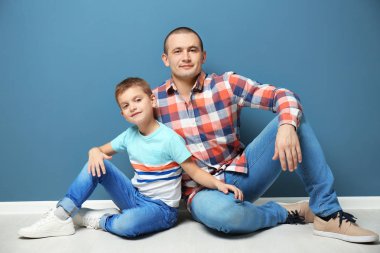 Baba ve oğlu renk duvarının yakınında katta oturan