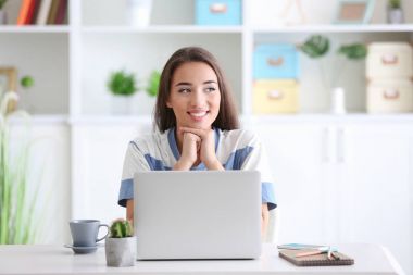 Kapalı masada otururken dizüstü bilgisayar kullanan genç kadın