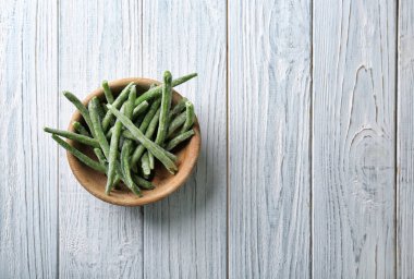 Ahşap arka plan üzerinde dondurulmuş yeşil fasulye ile kase