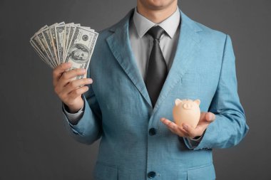 Businessman with dollar bills and piggy bank on grey background, closeup