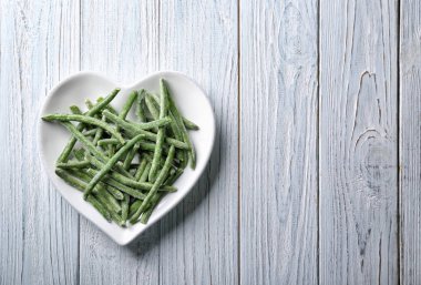 Dondurulmuş fasulye ahşap arka plan üzerinde kalp şeklinde plakalı