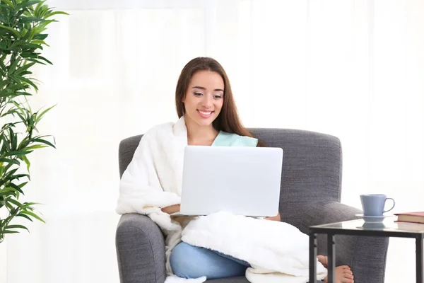 Jeune femme utilisant un ordinateur portable tout en étant assis sur un fauteuil à l'intérieur — Photo