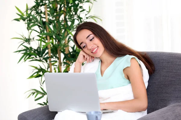 Young woman using laptop while sitting on armchair indoors — Stock Photo, Image