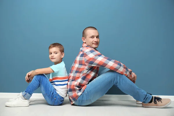 Vader en zoon zittend op de vloer in de buurt van kleur muur — Stockfoto