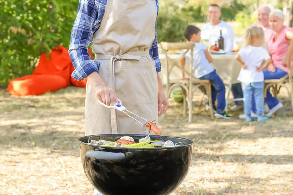 Femme cuisine des saucisses savoureuses avec des légumes sur barbecue grill en plein — Photo