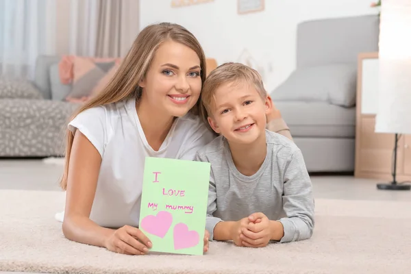 Ung kvinna med hennes lilla son och gratulationskort för mors dag hemma — Stockfoto