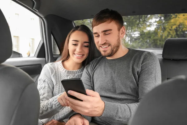 Felice giovane coppia con cellulare sul sedile posteriore di taxi auto — Foto Stock