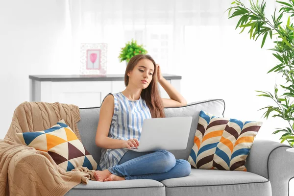 Молода жінка використовує ноутбук, сидячи на затишному дивані в приміщенні — стокове фото