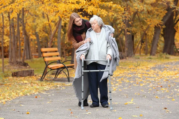 Senior woman with walking frame and young caregiver in park