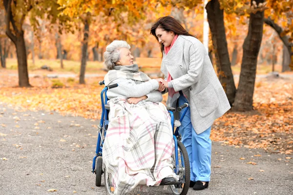 Gehandicapte senior vrouw en jonge groepsbegeleider in park — Stockfoto