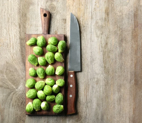 Board with fresh raw Brussels sprouts and knife on wooden background — Stock Photo, Image