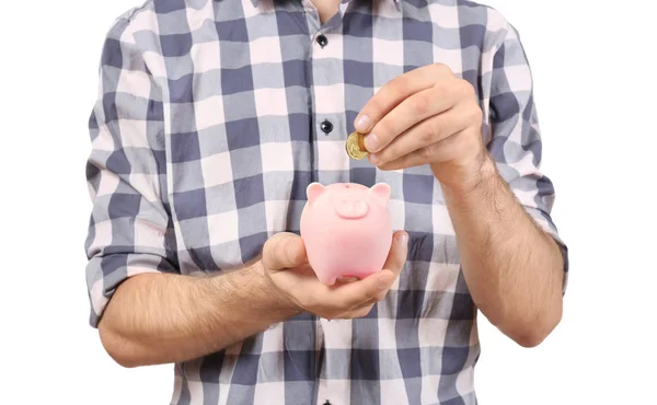 Jovem colocando moeda em porquinho banco no fundo branco, close-up — Fotografia de Stock