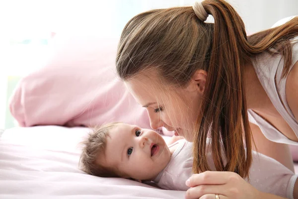 Jovem mãe e bebê bonito na cama em casa — Fotografia de Stock