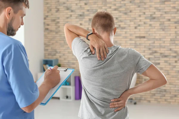 Physiotherapist with clipboard and young male patient in clinic — Stock Photo, Image
