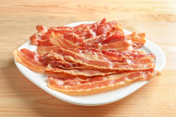 Placa con arandelas de tocino cocidas sobre mesa de madera —  Fotos de Stock