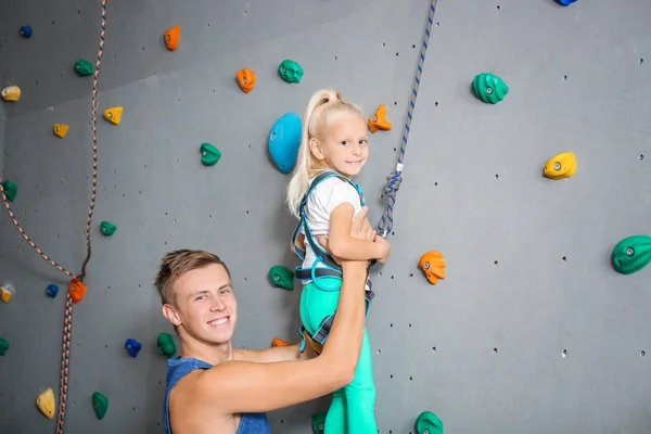 Instructeur helpt kleine meisje klim muur in sportschool — Stockfoto