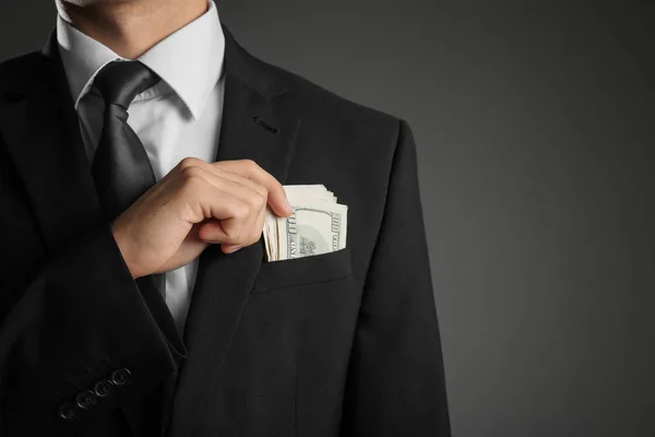 Jonge zakenman met dollarbiljetten in zak op een grijze achtergrond, close-up — Stockfoto