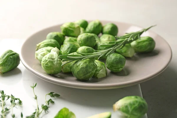 Tallrik med färsk rå brysselkål och örter på grå bord, närbild — Stockfoto