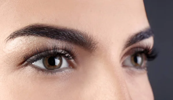 Beautiful young woman with eyelash extensions on grey background, closeup — Stock Photo, Image