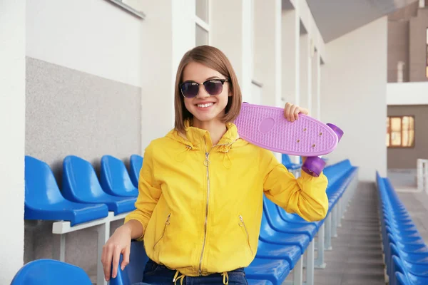 Hipster flicka med skateboard sitter på stol i arenan — Stockfoto