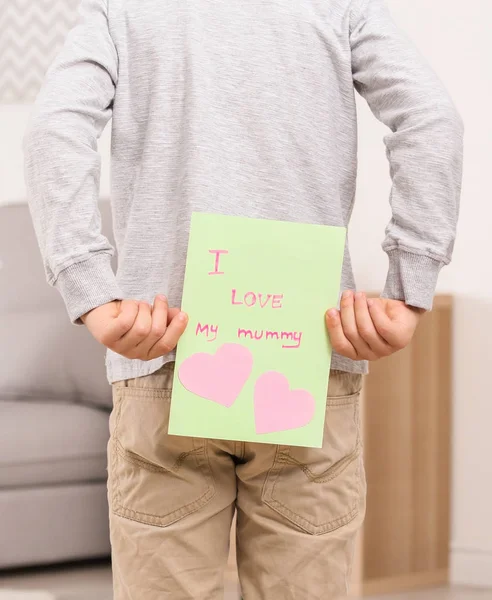 Lindo niño escondiendo la tarjeta de felicitación para el Día de la Madre a sus espaldas en casa —  Fotos de Stock