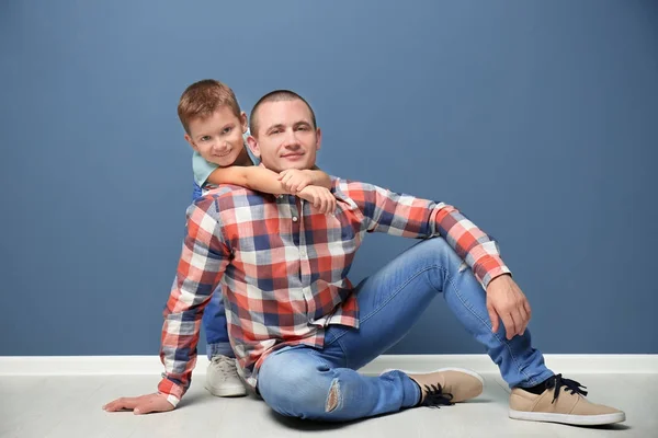 Vader en zoon zittend op de vloer in de buurt van kleur muur — Stockfoto