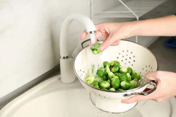 Woman washing raw Brussels sprouts in kitchen sink — Stock Photo, Image