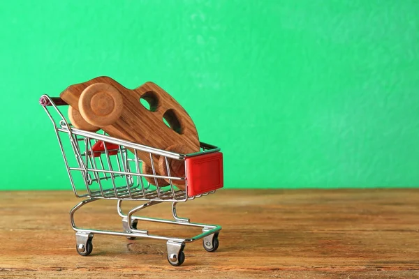 Wooden car and shopping cart on table against color background — Stock Photo, Image