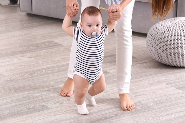 Mother helping her baby walk on floor at home