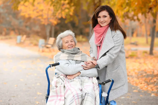 Disabled senior woman and young caregiver in park — Stock Photo, Image