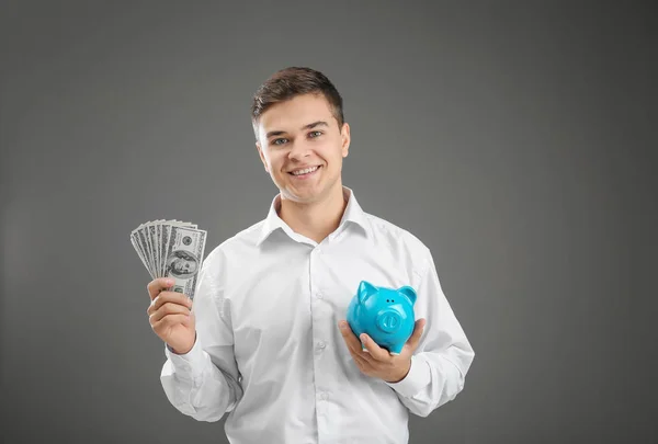 Giovane uomo d'affari con banconote in dollari e salvadanaio su sfondo grigio — Foto Stock