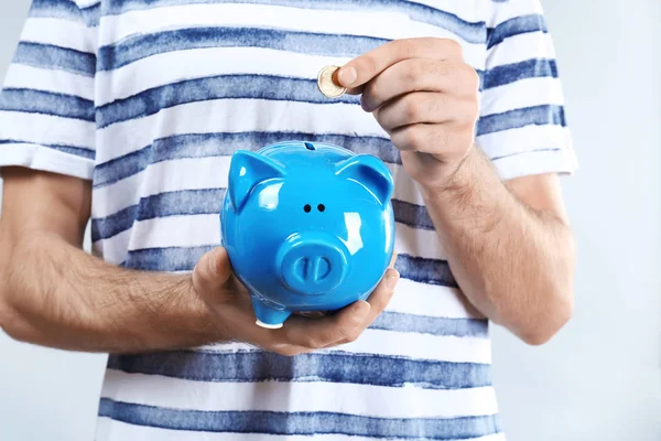 Jonge man brengen munt in piggy bank op lichte achtergrond, close-up — Stockfoto