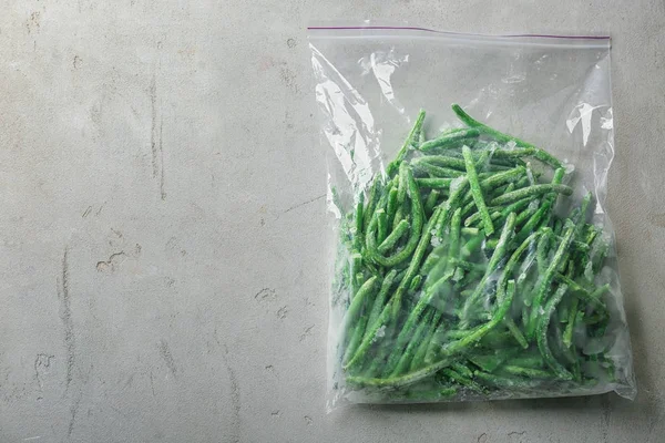 Műanyag zacskót a szürke háttér fagyasztott zöldbabbal — Stock Fotó