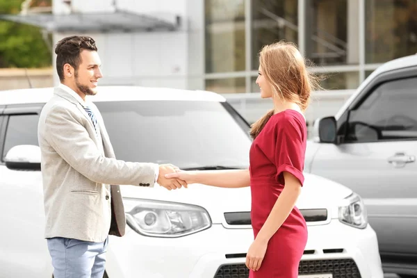 Customer and salesman shaking hands near new car outdoors — Stock Photo, Image