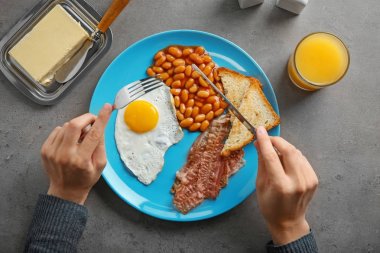 Young woman eating fried egg, bacon and beans at table clipart