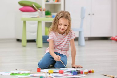 Küçük kız yerde evde otururken boyama