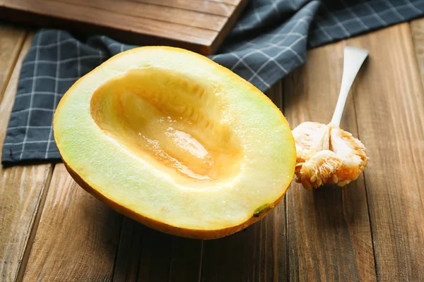 Leckere Melonenhälfte und Löffel mit Samen auf Holztisch — Stockfoto