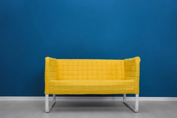 Sofá amarelo elegante no fundo da parede de cor — Fotografia de Stock