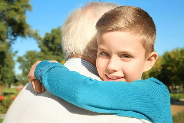 Cute little boy hugging grandfather outdoors — Stock Photo, Image