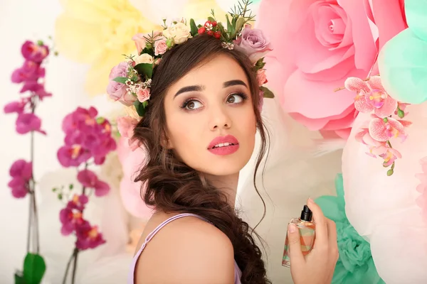 花で飾られた壁近くに立っている花の香水のボトルと美しい若い女性 — ストック写真