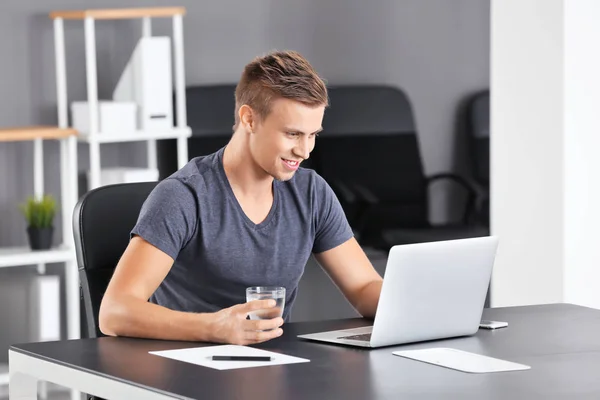 Przystojny mężczyzna z laptopa i szklanką wody w biurze — Zdjęcie stockowe