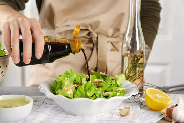 Женщина наливает соевый соус в миску со свежим салатом на столе — стоковое фото