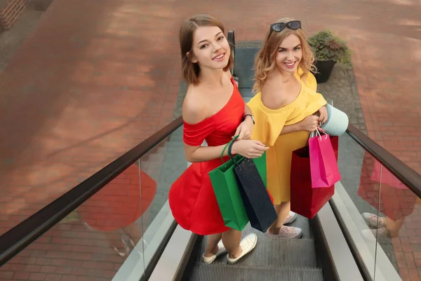 Mulheres bonitas com sacos de compras na escada rolante no shopping strip — Fotografia de Stock